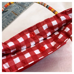 Detail view of red checkered fabric pouch with woven colorful handles and snap button