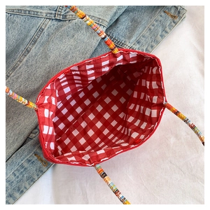 Detailed view of mobile phone bag featuring vibrant red checkered lining and woven handles