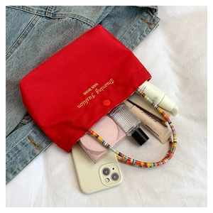 Detail of red canvas phone bag featuring colorful beaded handle and makeup storage space