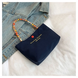 Detail of navy canvas handbag featuring colorful beaded handle and golden embroidery