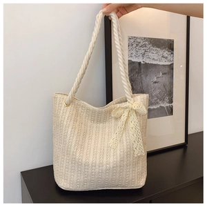Detail of beige woven straw tote bag featuring rope handles and delicate lace bow