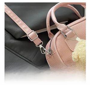 Close-up of pink litchi grain leather bag with silver metal hooks and plush ball charm