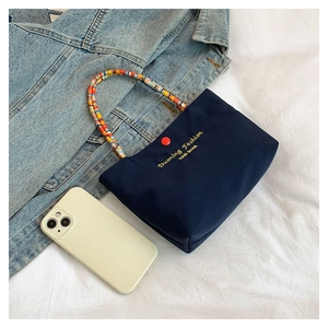 Detail of navy canvas handbag with a bold red button and vibrant beaded handle
