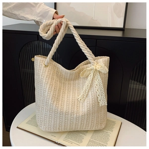 Detailed texture of woven straw tote bag featuring white lace bow and rope handle