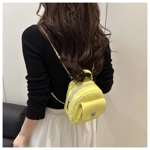 Model wearing yellow quilted mini backpack with leather-interwoven chain strap detail