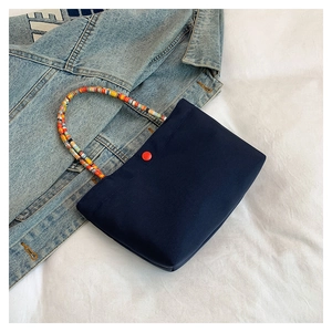 Detail of navy canvas phone bag with colorful beaded handle and red button closure