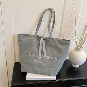 Minimalist grey canvas tote bag with embroidery, styled on a modern bookshelf setting