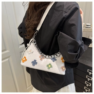 Detail of white crocodile texture baguette bag with colorful plush flower charms and chain