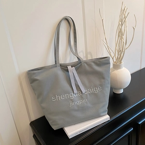 Minimalist grey canvas tote bag with textured embroidery on a stylish shelf display