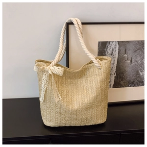 Detail of beige straw tote bag featuring white cotton rope handles and lace bow accent