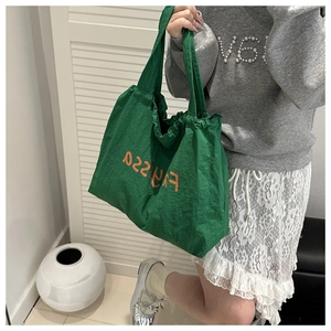 Detail of green nylon tote bag with drawstring closure and orange letter logo detail