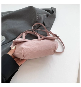 Detail of pink washed nylon handbag featuring bow design and adjustable shoulder strap