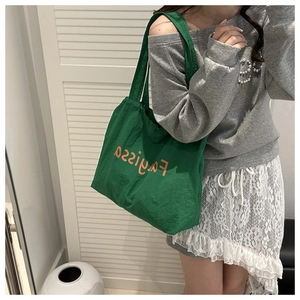 Detail of green canvas tote bag with orange lettering worn on a model's shoulder