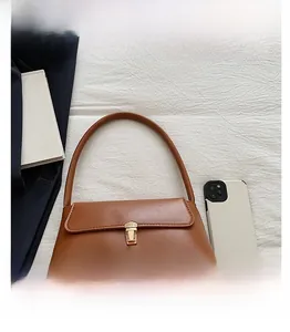 Détail d'un sac baguette marron caramel avec boucle dorée sur un tissu texturé blanc
