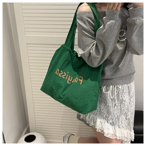 Lifestyle shot of large green tote bag with orange lettering worn over the shoulder