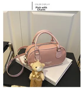 Pink bowling bag with cute bear charm on books, showcasing grainy texture and strap
