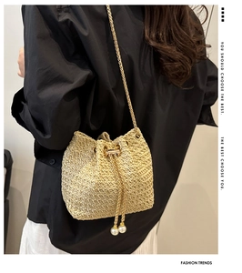 Detail of woven beige straw bucket bag with gold chain strap and pearl drawstring accents