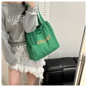 Mirror selfie showing a green tote bag with orange lettering and textured fabric