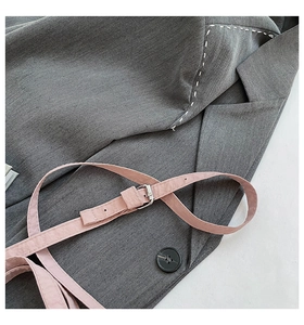 Detail of grey blazer fabric featuring a pink accent belt and white contrast stitching