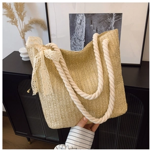 Close-up of woven straw tote bag featuring white cotton rope handles and lace bow detail