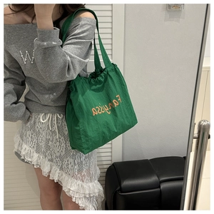 Detail view of emerald green nylon tote bag featuring orange lettering and drawstring design