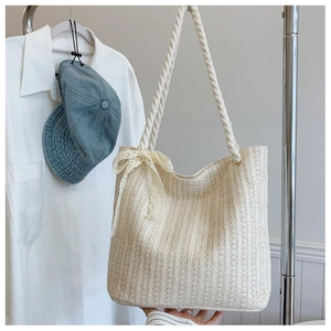 Detail of a large beige straw woven tote bag featuring decorative lace bows and rope handles