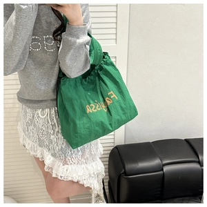 Mirror selfie showing a green nylon drawstring handbag with orange artistic lettering