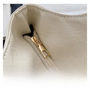 Close-up of smooth gold metal zipper on cream white pebble grain leather tote bag