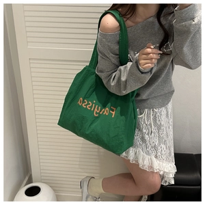 Detail of a large green canvas tote bag with orange lettering worn by a model