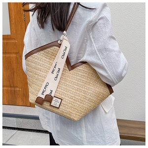 Detail of hand-woven straw tote bag with brown faux leather trim and wide fabric strap