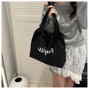 Detail of black drawstring nylon tote bag featuring white artistic lettering and ribbon handles