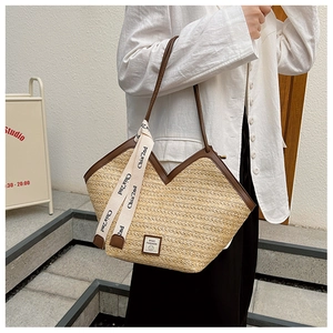 Detail view of woven straw tote bag with brown leather trim and decorative webbing strap