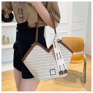 Detail of straw tote bag with brown leather straps and decorative ribbon on handle