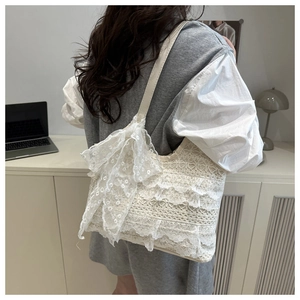 Détail du sac cabas en dentelle blanche avec un grand nœud et broderie sur la bandoulière