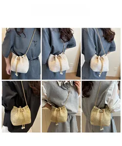 Detail view of woven bucket bag featuring gold chain strap and elegant pearl charm