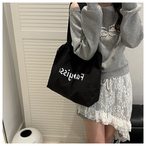 Detail of a large black nylon tote bag featuring a drawstring closure and white logo lettering