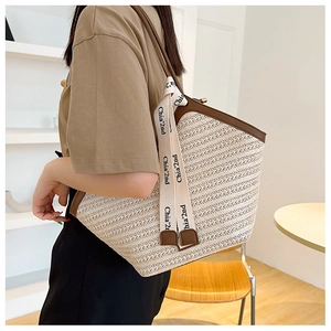 Side view of woman carrying a beige woven tote bag with brown leather trim and canvas strap