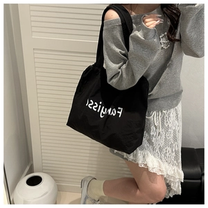 Model wearing a large black canvas tote bag with white artistic lettering for commute