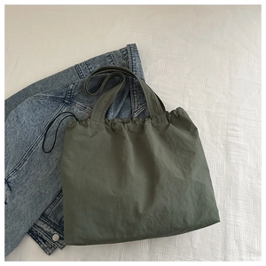 Top view of olive green drawstring canvas tote bag on white linen with denim jacket