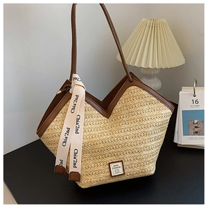Detail of straw tote bag with brown leather trim, decorative ribbon, and logo patch