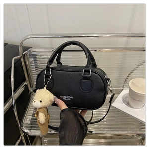 Detail of black litchi grain leather handbag with cute white bear plush charm on a rack