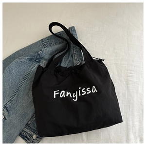 Flat lay of black canvas tote bag with drawstring closure on a bed with denim jacket