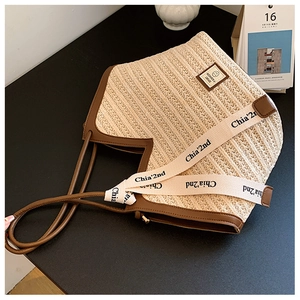 Detail of woven straw tote bag with brown leather handles and decorative branded ribbon