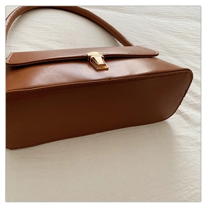 Gros plan du sac sous l'aisselle en cuir marron avec boucle dorée et coutures détaillées