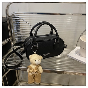 Detailed shot of black litchi leather bowling bag with cute teddy bear charm on metal shelf