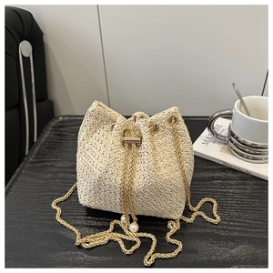 Detail of cream woven bucket bag with gold chain strap and pearl accents on wooden table
