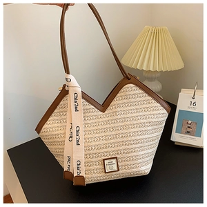 Close-up of woven straw tote bag with brown leather trim and decorative ribbon detail