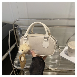 Detail of beige lychee grain leather boston bag featuring a cute teddy bear charm