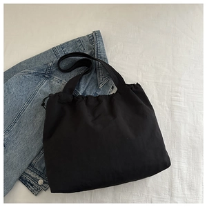 Detail view of black nylon drawstring tote bag with thick strap on white checkered background