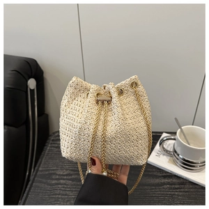 Detail of cream woven bucket bag showing gold drawstring closure and metal chain strap